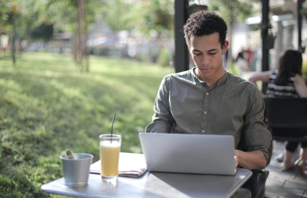 black man using a laptop in the park with a beverage outside