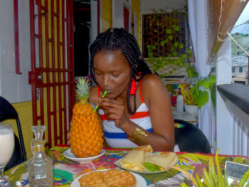 black girl sipping a pina colada with african clothes at an island food caribbean restaurant in Dominica