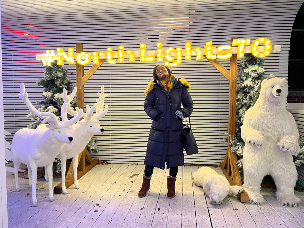 Beautiful black girl posing with white reindeers and polar bears at a christmas lights exhibition - Things to do in Toronto in December