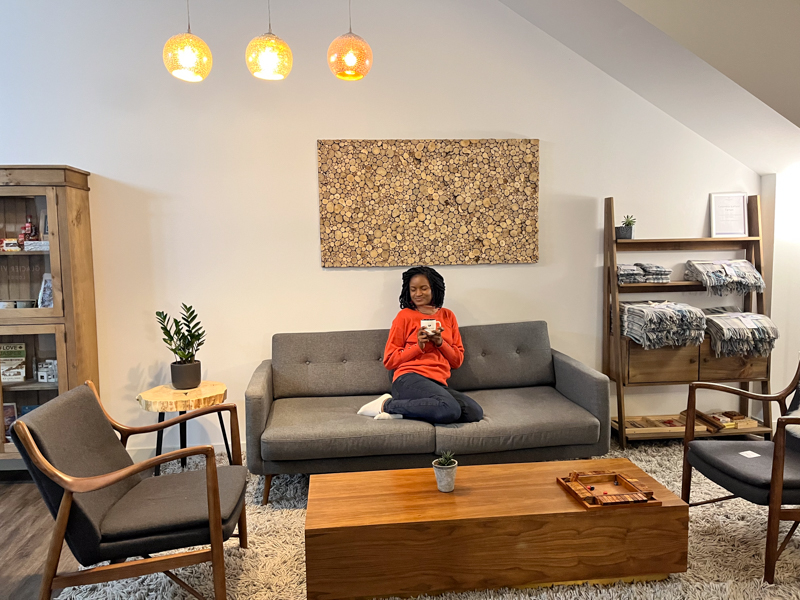 Black woman with braids wearing an orange sweater and having some relaxing tea at the Moraine lounge at the Glacier View Lodge 