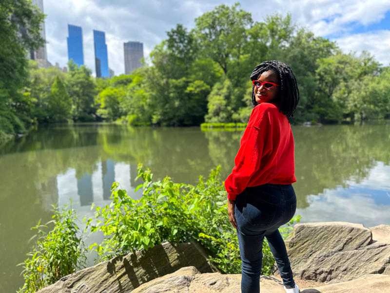 Black girl posing in a red sweater and showing beautiful views of Central Park during a New York City Summer