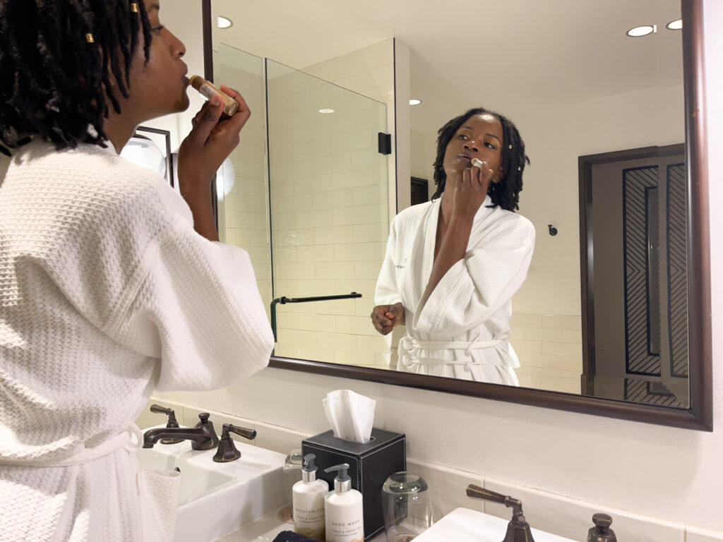 Black girl applying a lip balm from Bee Natural, a sustainable beauty brand from Dominica, while staying at the River Terrace Inn, a downtown Napa hotel