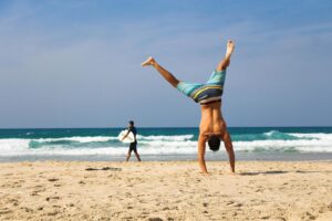 man doing a handstand - man holding a surfboard