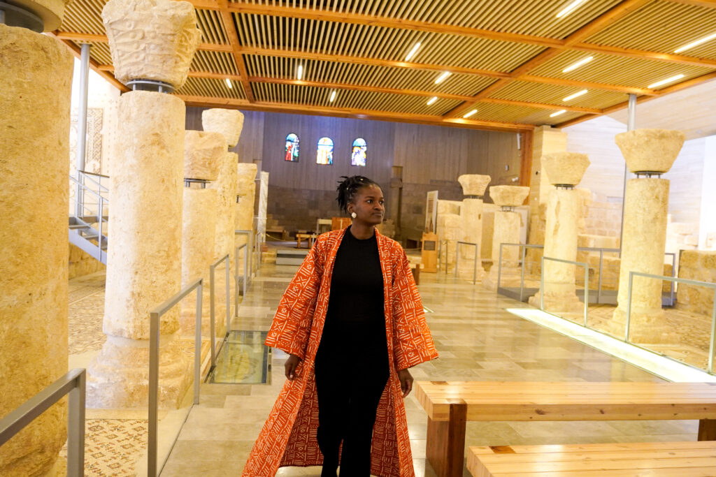What to wear in Jordan - Black female influencer, Travel with Clem, wearing a beautiful brown bogolan coat from the Ngaska store while exploring the church at the Mount Nebo site in Jordan