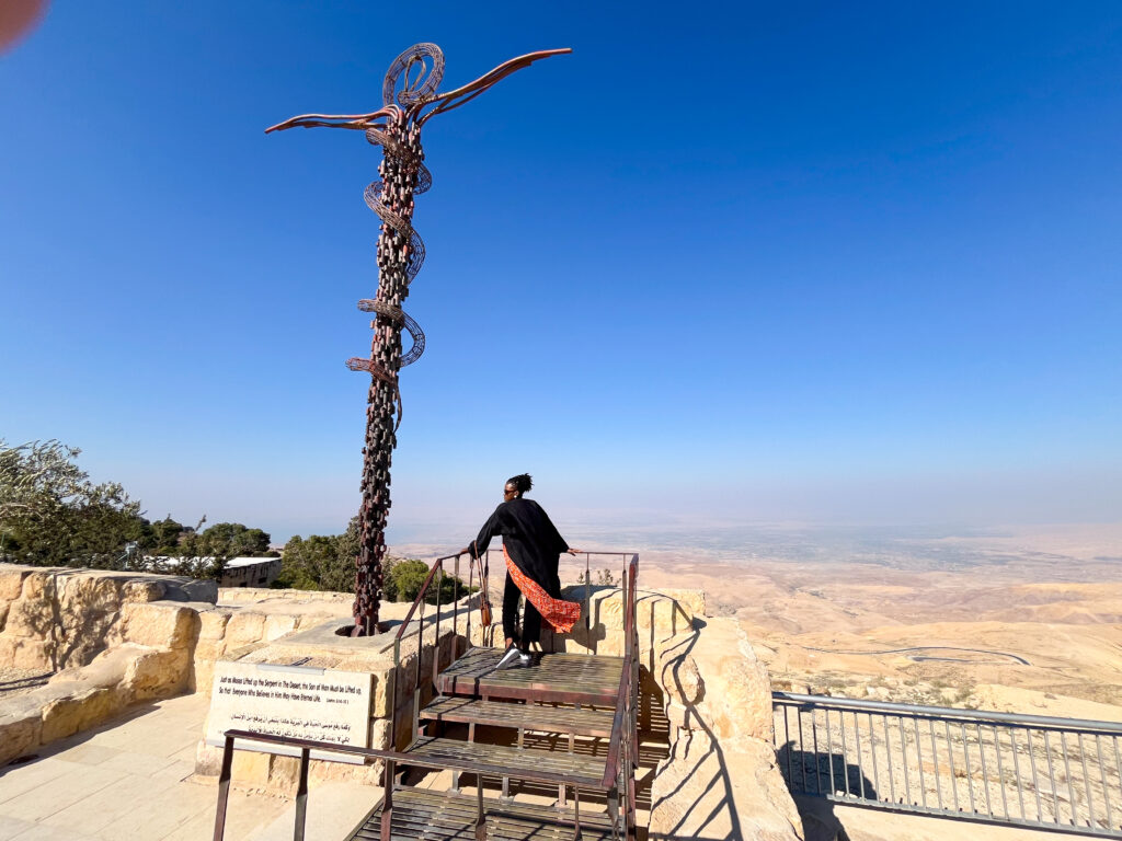 Travel with Clem, beautiful black influencer posing next to Moses staff (sign of medicine) at Mount Nebo in Jordan