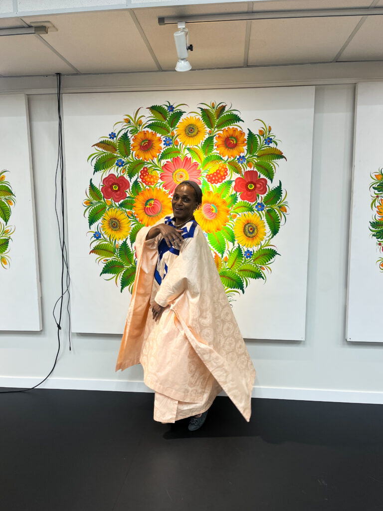 Gislaine Ada Ngaska, the mother of Travel with Clem, posing in front of a beautiful flower painting at the Ukrainian Museum of Canada
